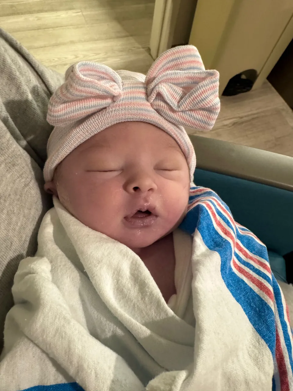 Andie Brooke as a newborn, sleeping peacefully, swaddled in a hospital blanket and wearing a striped knit hat with a bow